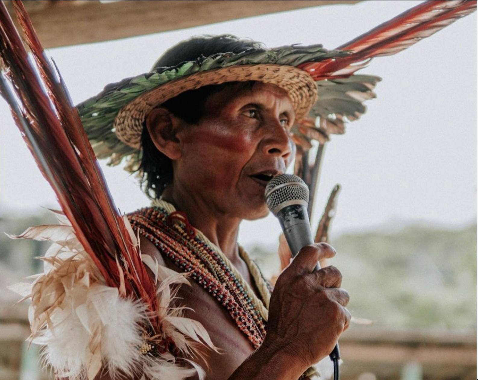 An Indigenous Amazonian man speaking into a microphone in traditional dress