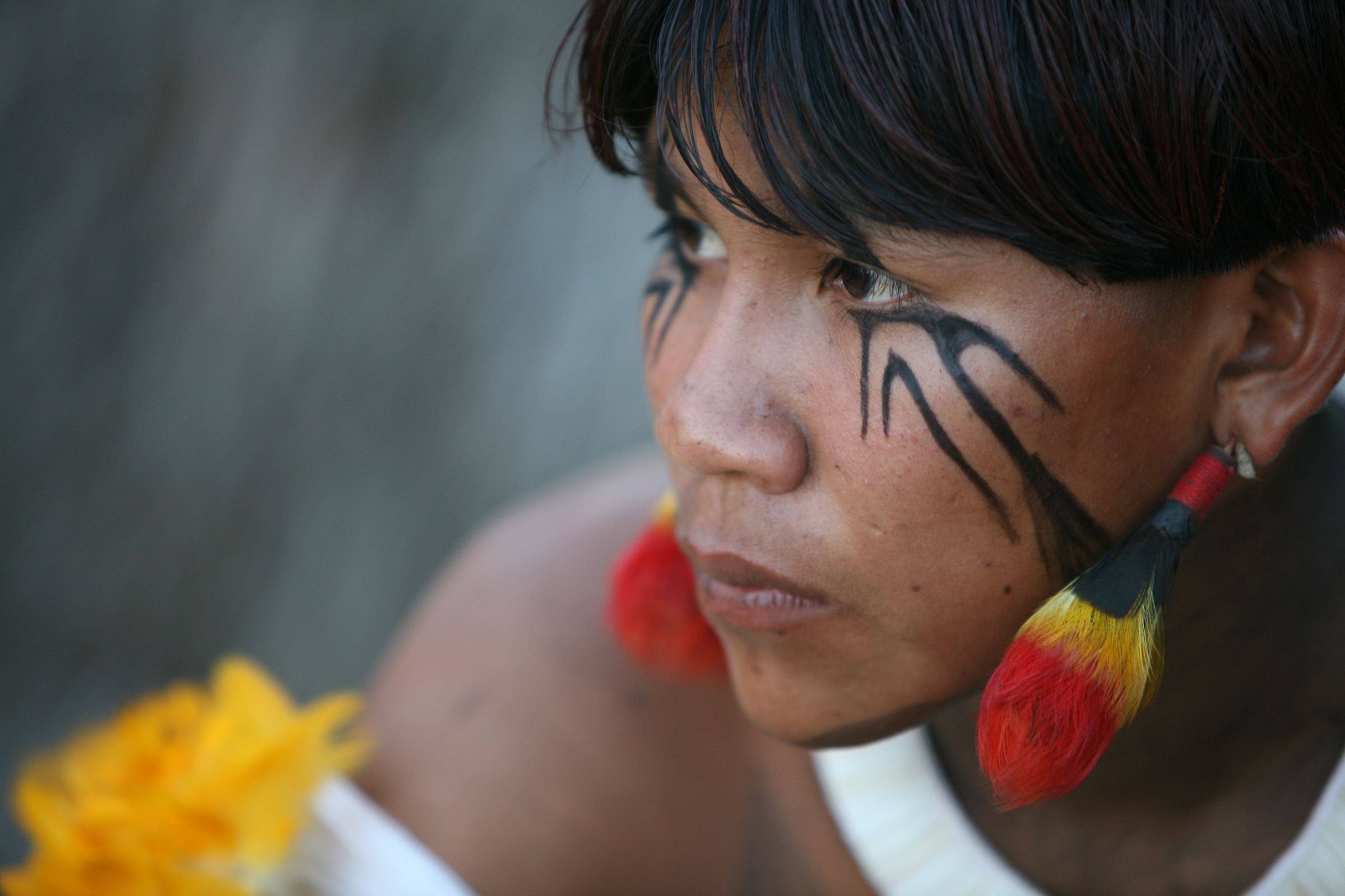 A young person from the Xingu region of Brazil, face painted in black, with feathered earrings